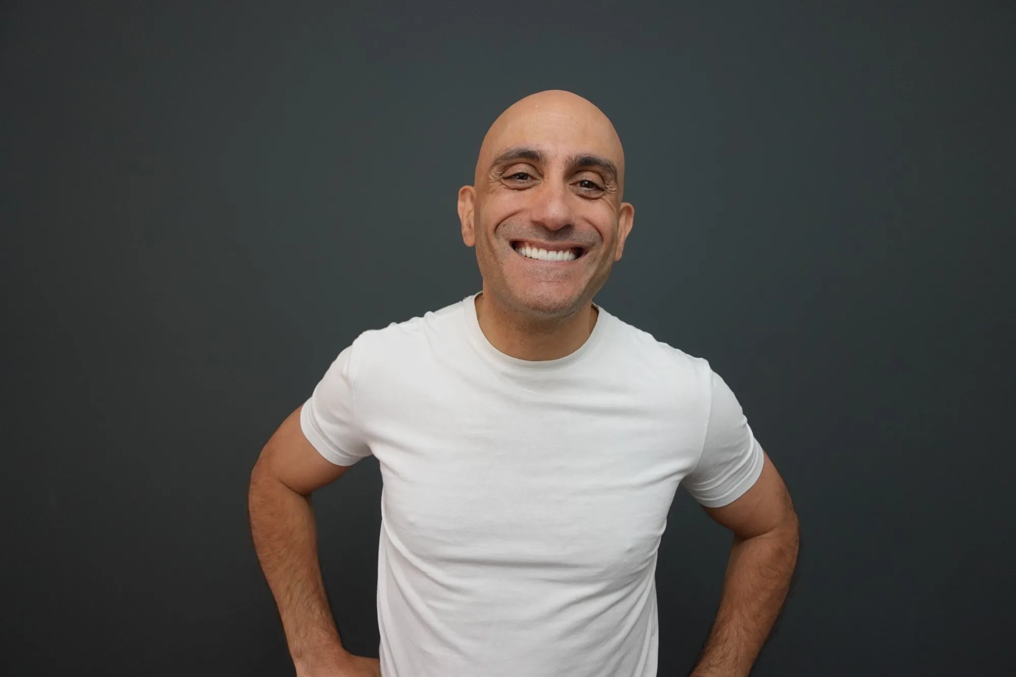Chris K smiling, hands on hips, against a dark studio backdrop